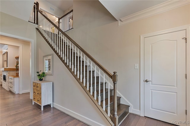 staircase featuring visible vents, baseboards, crown molding, and wood finished floors