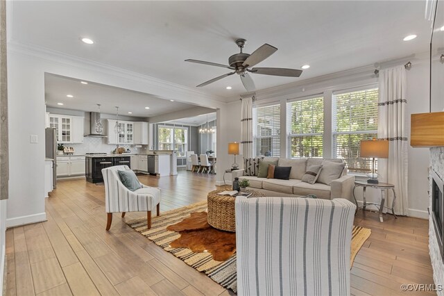 living room with ornamental molding, a stone fireplace, recessed lighting, a ceiling fan, and light wood-style flooring