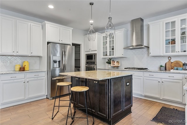 kitchen featuring white cabinets, appliances with stainless steel finishes, light wood-style flooring, and wall chimney exhaust hood