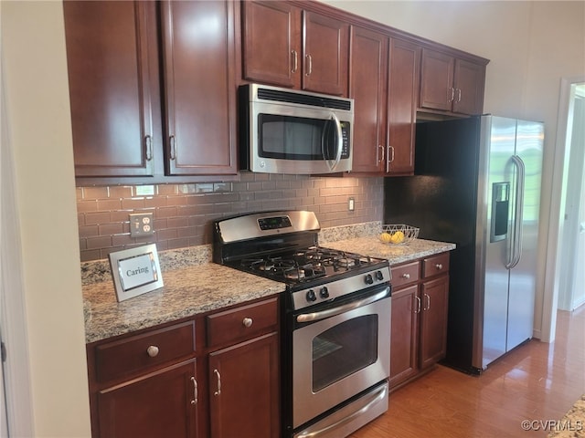 kitchen with light wood-style flooring, appliances with stainless steel finishes, light stone countertops, and tasteful backsplash