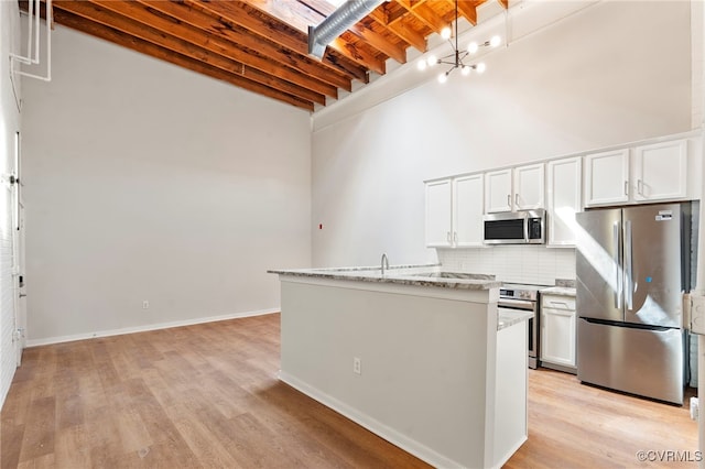 kitchen with appliances with stainless steel finishes, tasteful backsplash, light stone counters, beamed ceiling, and a high ceiling