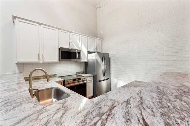 kitchen with decorative backsplash, appliances with stainless steel finishes, light stone countertops, a sink, and white cabinets