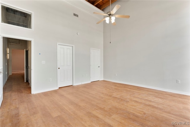 unfurnished room with ceiling fan, light wood finished floors, baseboards, a towering ceiling, and visible vents