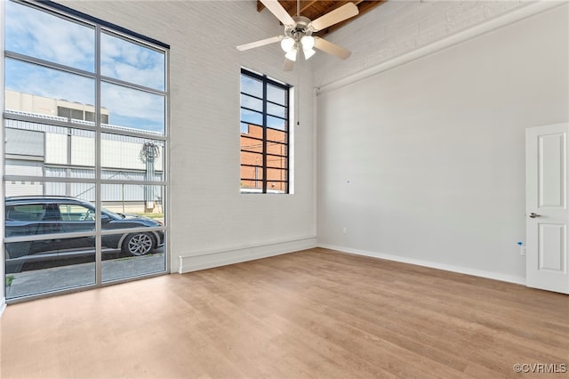 empty room featuring baseboards, a ceiling fan, a high ceiling, and wood finished floors