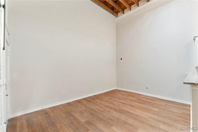 unfurnished room with baseboards, beam ceiling, and light wood-style floors