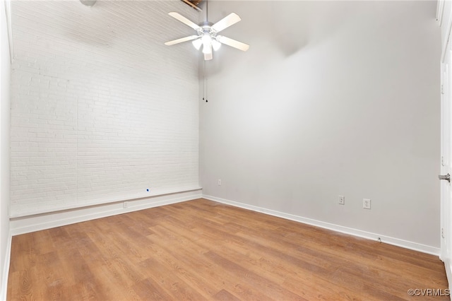 empty room featuring baseboards, ceiling fan, wood finished floors, and brick wall