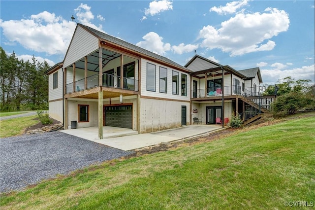 back of property with french doors, driveway, an attached garage, a lawn, and stairs