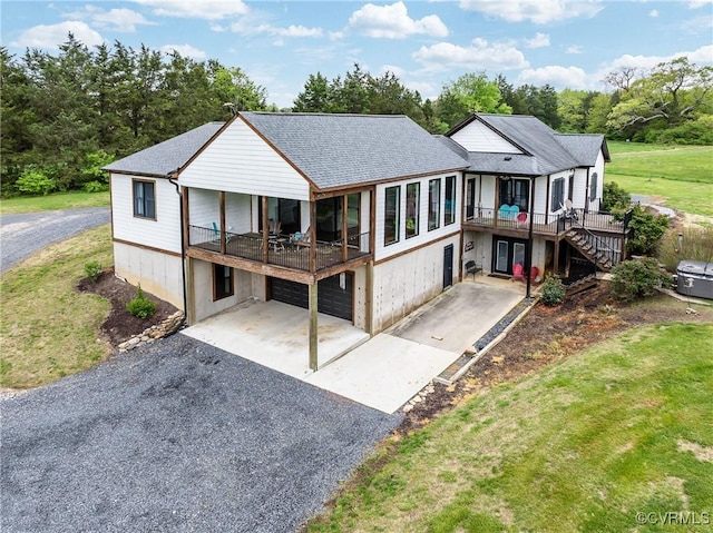 back of house featuring stairway, aphalt driveway, a shingled roof, a yard, and an attached garage