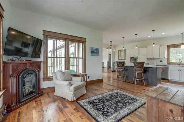 living room with baseboards, light wood-style flooring, a glass covered fireplace, and recessed lighting