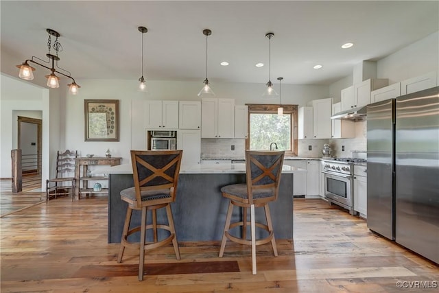 kitchen featuring white cabinets, stainless steel appliances, tasteful backsplash, under cabinet range hood, and a kitchen island