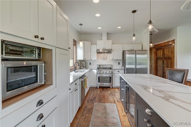kitchen with a sink, hardwood / wood-style flooring, appliances with stainless steel finishes, white cabinetry, and under cabinet range hood