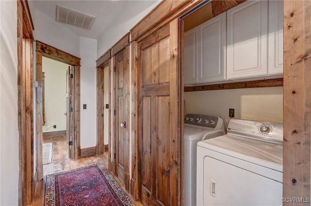 clothes washing area with washer and dryer, cabinet space, wood finished floors, and visible vents