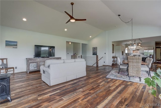living area with dark wood finished floors, vaulted ceiling, a wood stove, and a ceiling fan