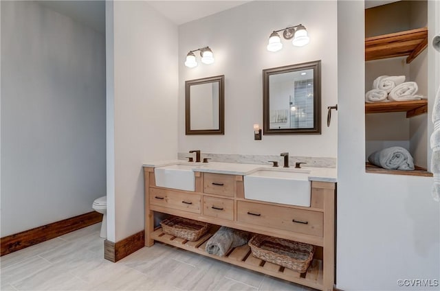 full bathroom featuring baseboards, a sink, double vanity, and toilet