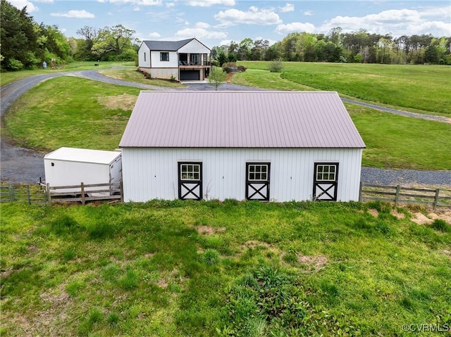 view of barn with an exterior structure, a lawn, a rural view, and fence