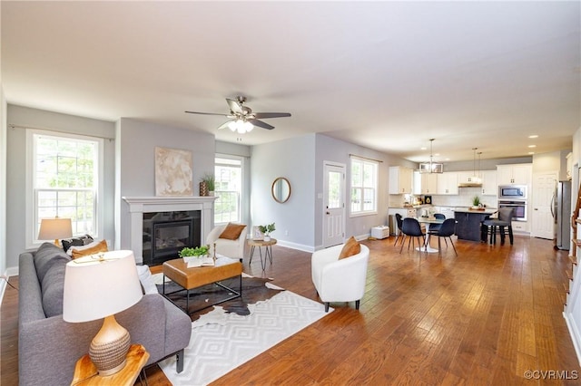 living area with baseboards, dark wood finished floors, a glass covered fireplace, and a healthy amount of sunlight