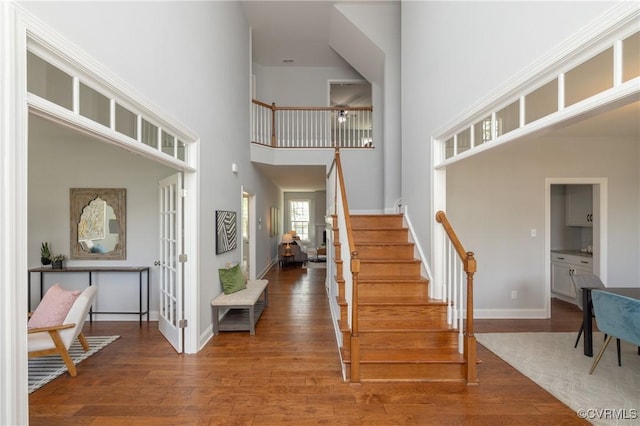 entrance foyer with baseboards, a high ceiling, wood finished floors, and stairway