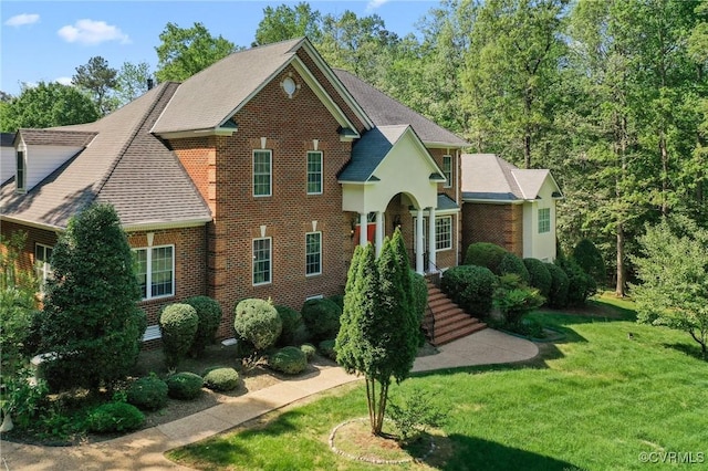 view of front of property with a front lawn, a shingled roof, and brick siding