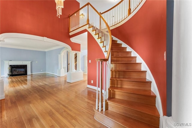 staircase featuring baseboards, wood finished floors, arched walkways, and a towering ceiling