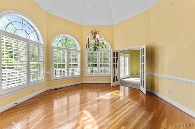 unfurnished dining area with a chandelier, french doors, baseboards, wood finished floors, and high vaulted ceiling