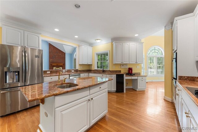kitchen with a sink, light wood-style flooring, light stone counters, white cabinets, and appliances with stainless steel finishes