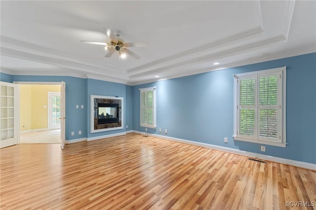unfurnished living room with light wood-type flooring, a raised ceiling, and a healthy amount of sunlight