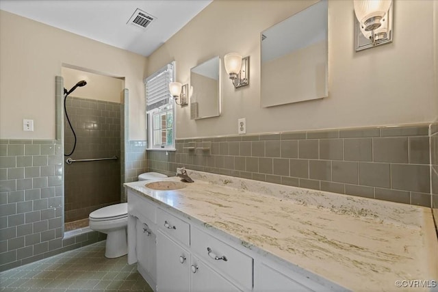 bathroom with tile patterned floors, toilet, visible vents, tile walls, and a tile shower