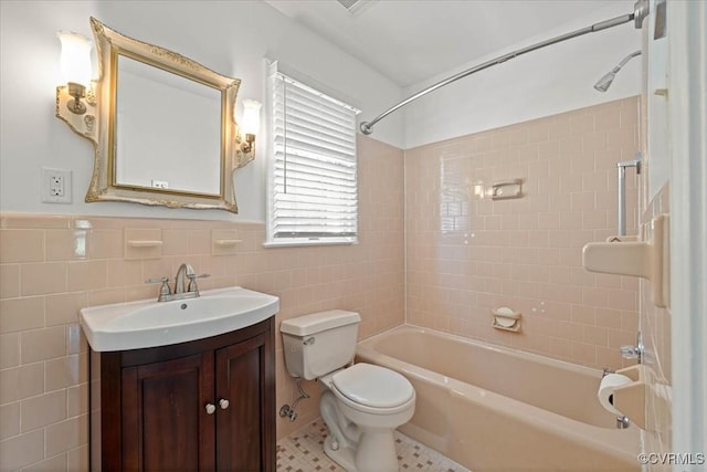 bathroom featuring toilet, tile walls, wainscoting, vanity, and bathing tub / shower combination