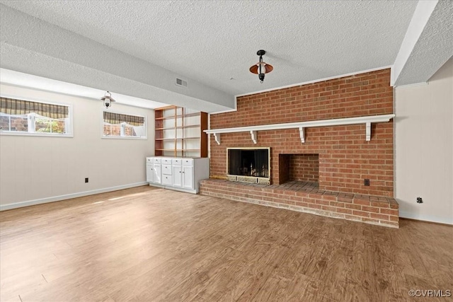 unfurnished living room with visible vents, baseboards, a brick fireplace, a textured ceiling, and wood finished floors