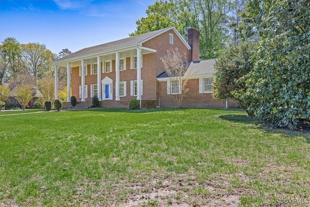 neoclassical / greek revival house featuring brick siding, a porch, a front lawn, and a chimney