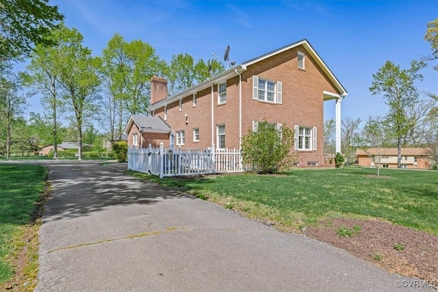 view of side of home featuring a chimney, aphalt driveway, brick siding, fence, and a lawn