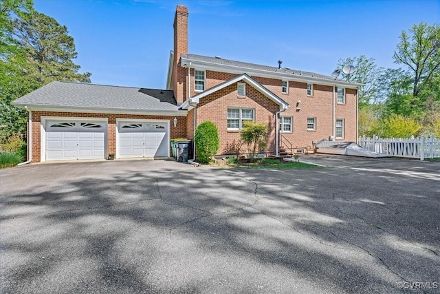 view of front facade with an attached garage, driveway, fence, and brick siding