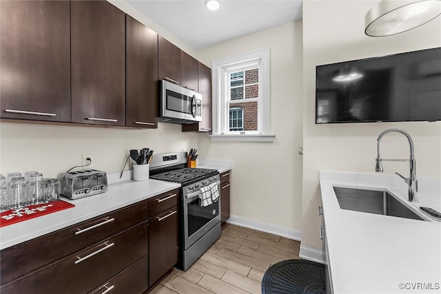kitchen featuring appliances with stainless steel finishes, a sink, light countertops, baseboards, and wood finish floors