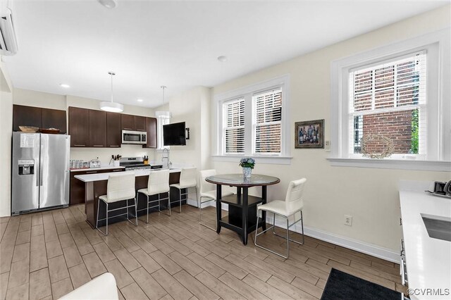 kitchen featuring stainless steel appliances, dark brown cabinets, light countertops, a breakfast bar area, and light wood-type flooring