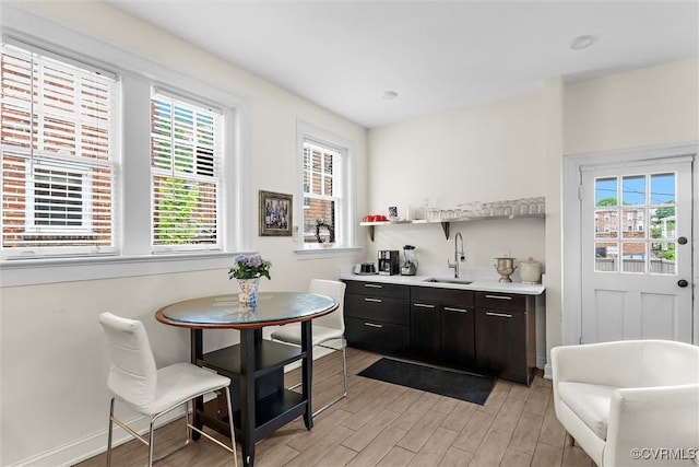 kitchen with a sink, light wood-type flooring, light countertops, baseboards, and open shelves
