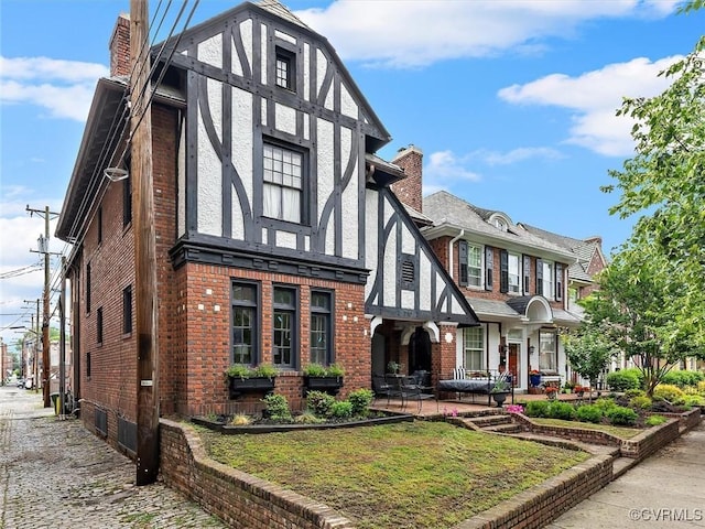 tudor home featuring a chimney and brick siding
