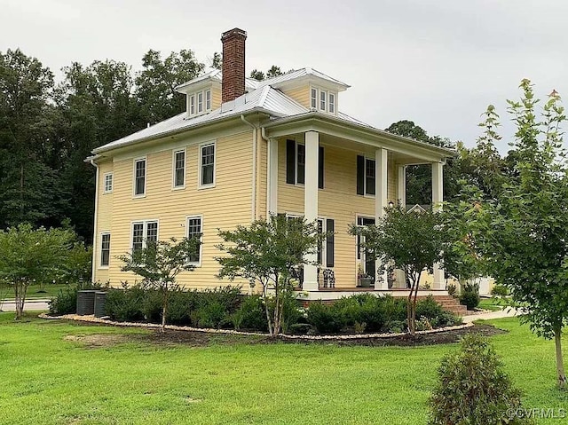 view of side of property featuring covered porch, a lawn, and a chimney