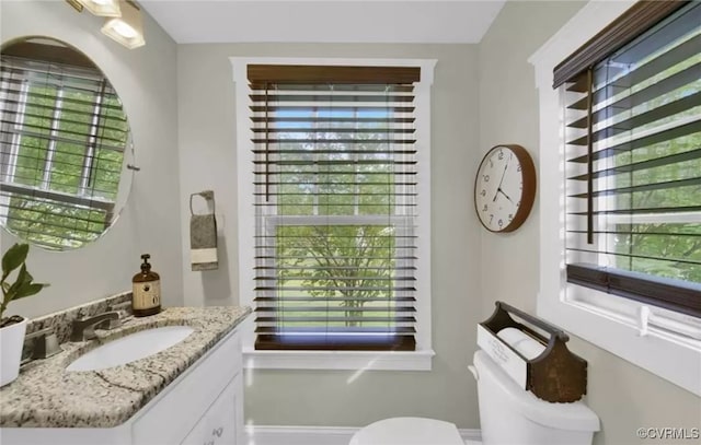 bathroom with baseboards, vanity, toilet, and a wealth of natural light