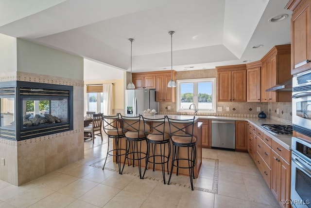 kitchen featuring stainless steel appliances, a tray ceiling, light tile patterned flooring, and a kitchen bar