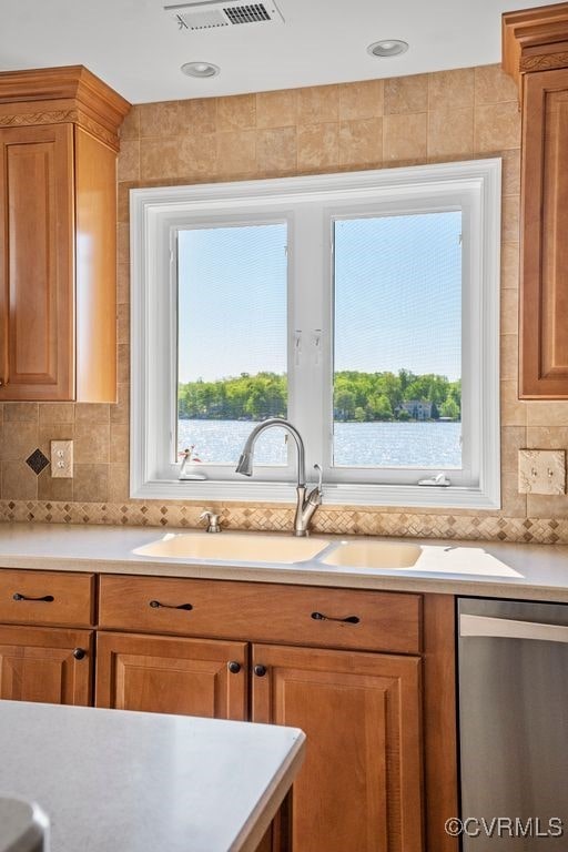 kitchen featuring a sink, dishwasher, light countertops, brown cabinetry, and visible vents