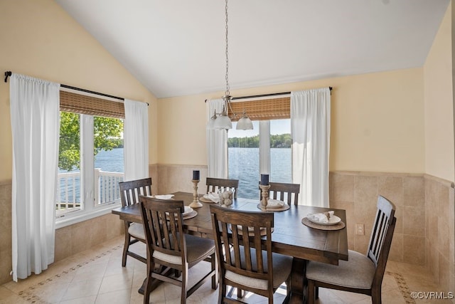 dining space with light tile patterned flooring, vaulted ceiling, wainscoting, and a water view