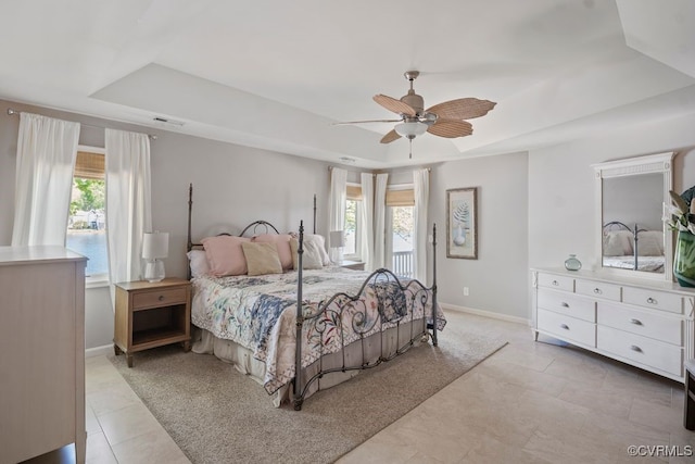 bedroom with a tray ceiling, visible vents, multiple windows, and baseboards