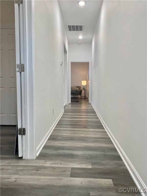 hallway featuring visible vents, baseboards, and wood finished floors