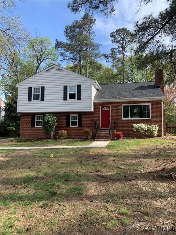 split level home featuring entry steps, a front lawn, a chimney, and brick siding