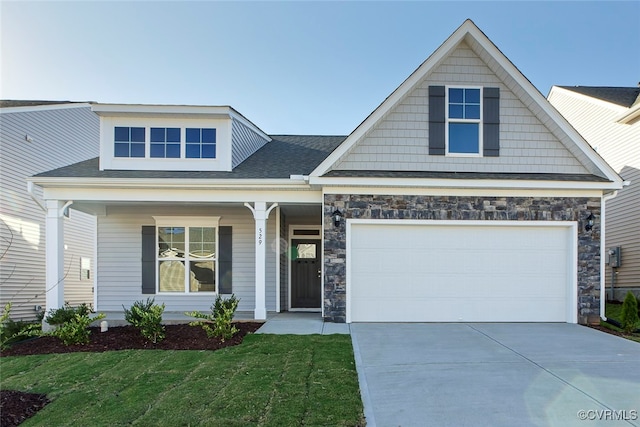 view of front facade featuring driveway, covered porch, a front yard, a garage, and stone siding