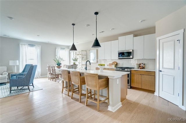 kitchen with light countertops, a center island with sink, stainless steel appliances, and light wood finished floors