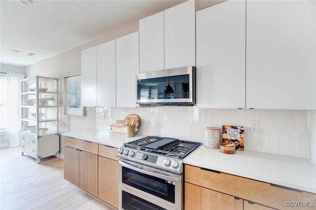 kitchen featuring light countertops, appliances with stainless steel finishes, decorative backsplash, and light wood-style flooring