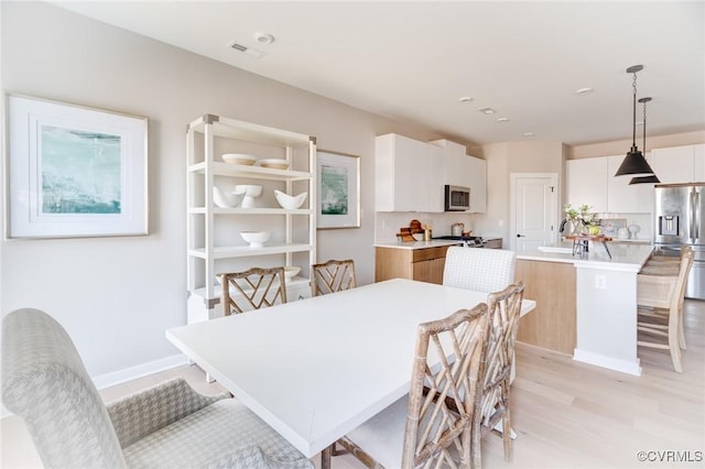 dining area with visible vents, light wood-style floors, and baseboards