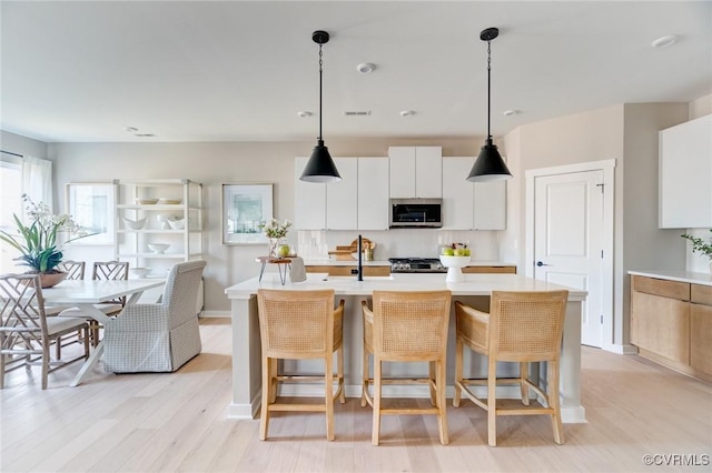 kitchen with a center island with sink, light countertops, white cabinets, stainless steel microwave, and a breakfast bar