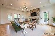 living room with wood finished floors, ornamental molding, a stone fireplace, and a notable chandelier